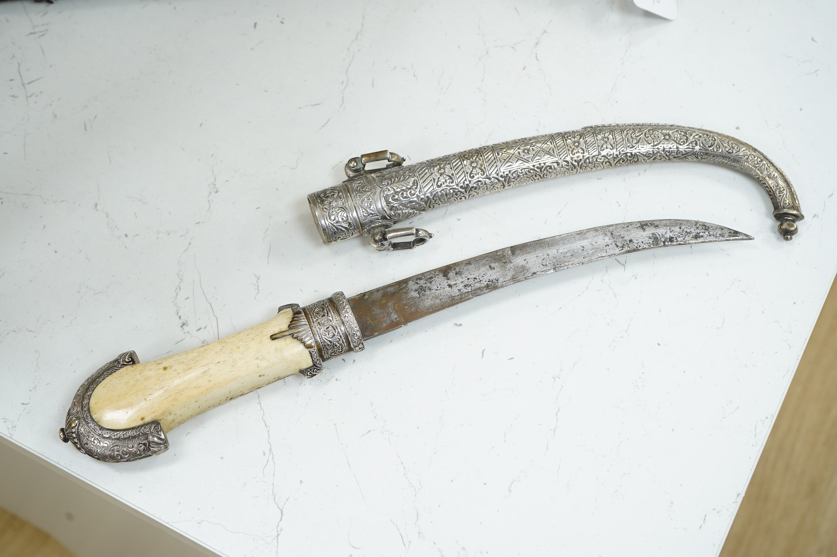A silver mounted Moroccan dagger jambya, with silver sheath and hilt, mounts chased with foliate and floral designs, and one piece bone grip, blade as found, overall length 42cm
